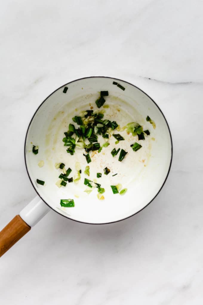 A white pot with sautéed green onions in it