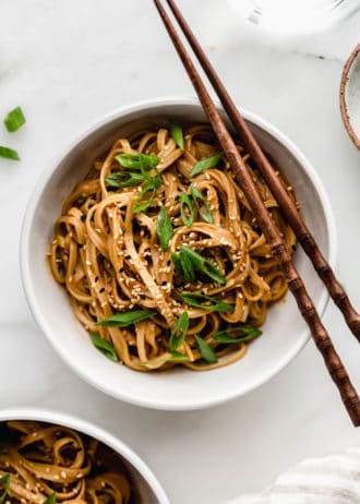 A bowl of peanut butter noodles with wooden chopsticks on the side