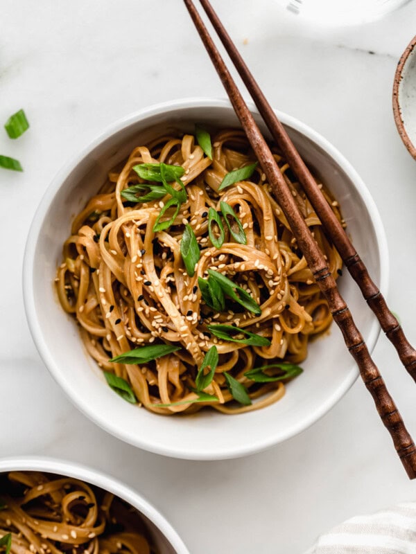 A bowl of peanut butter noodles with wooden chopsticks on the side