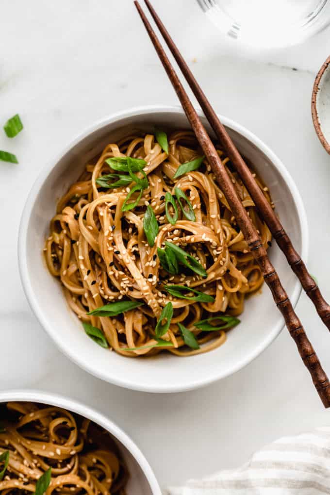 A bowl of peanut butter noodles with wooden chopsticks on the side