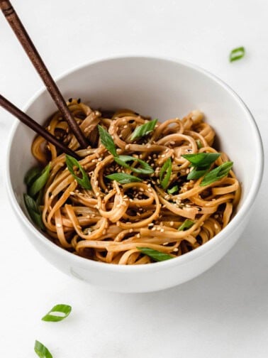 Peanut butter noodles in a white bowl topped with green onions