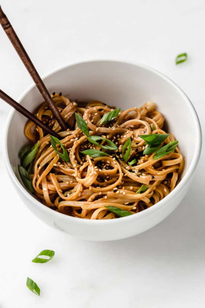 Peanut butter noodles in a white bowl topped with green onions