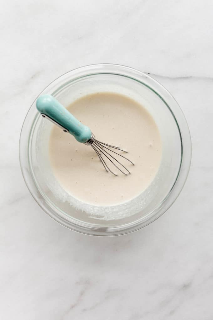 Coconut milk in a clear mixing bowl with a whisk