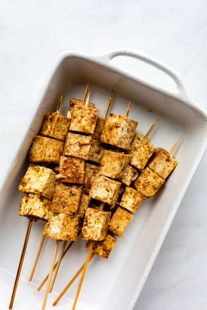 uncooked tofu satay skewers in a white baking dish