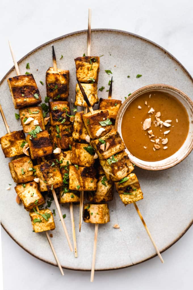 a plate of tofu satay skewers with a side of peanut butter sauce