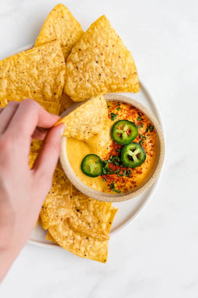 a hand dipping a tortilla chip into a bowl of vegan queso