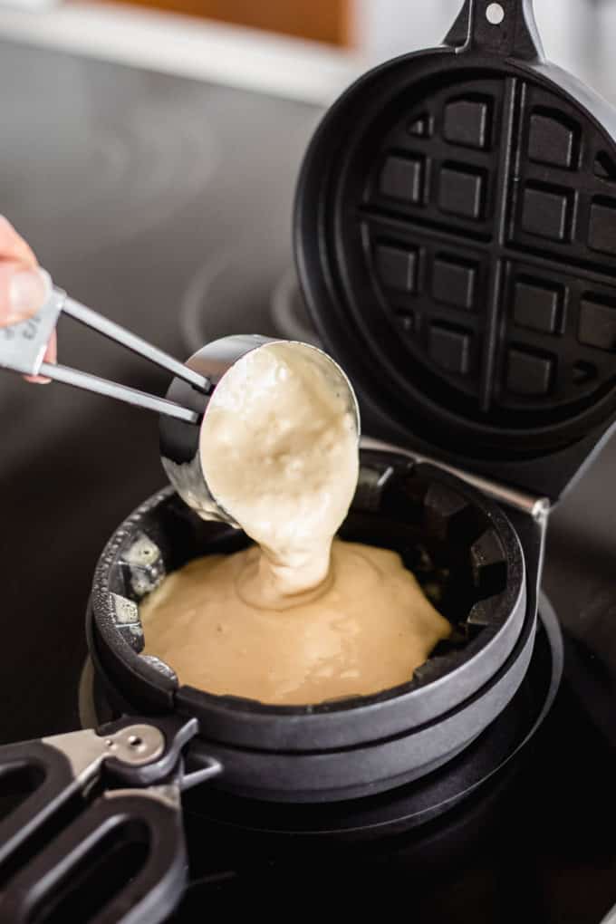 a measuring cup pouring batter into a waffle iron
