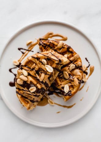 a waffle cut in half on a plate with peanuts and drizzled chocolate on it