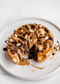 a waffle cut in half on a plate topped with drizzled peanut butter and chocolate