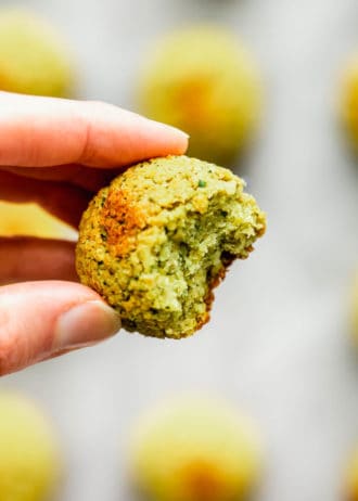 a hand holding a baked falafel ball with a bite taken out of it