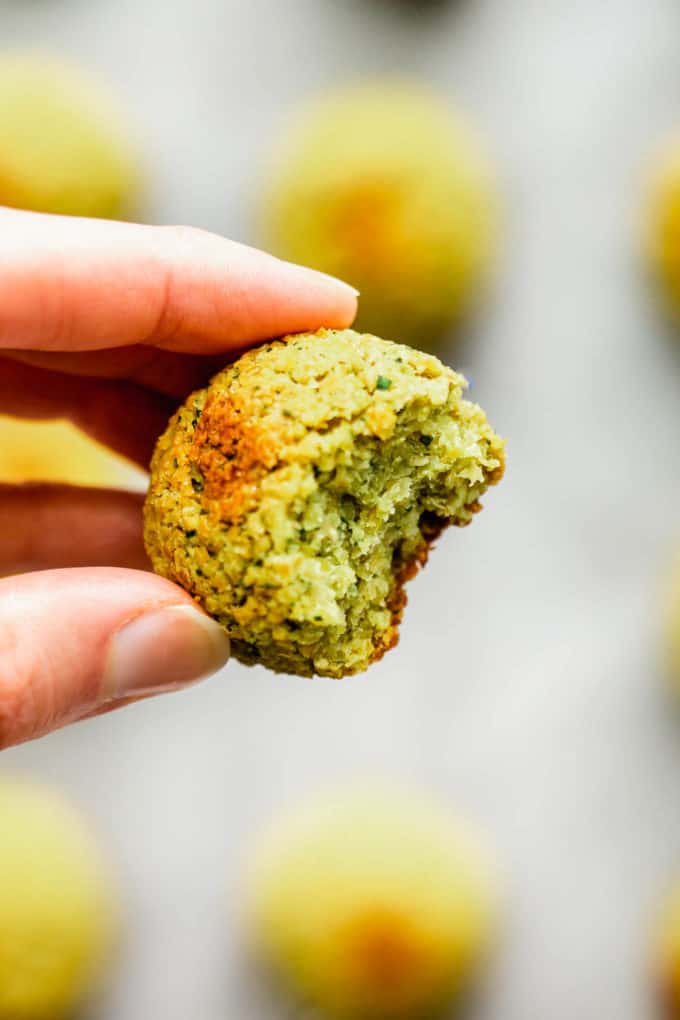 a hand holding a baked falafel ball with a bite taken out of it