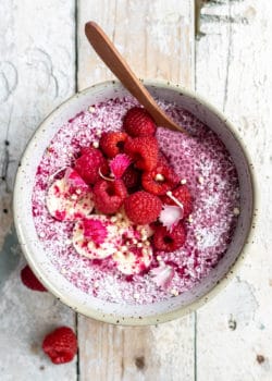 raspberry chia pudding in a white speckled bowl with a spoon in it