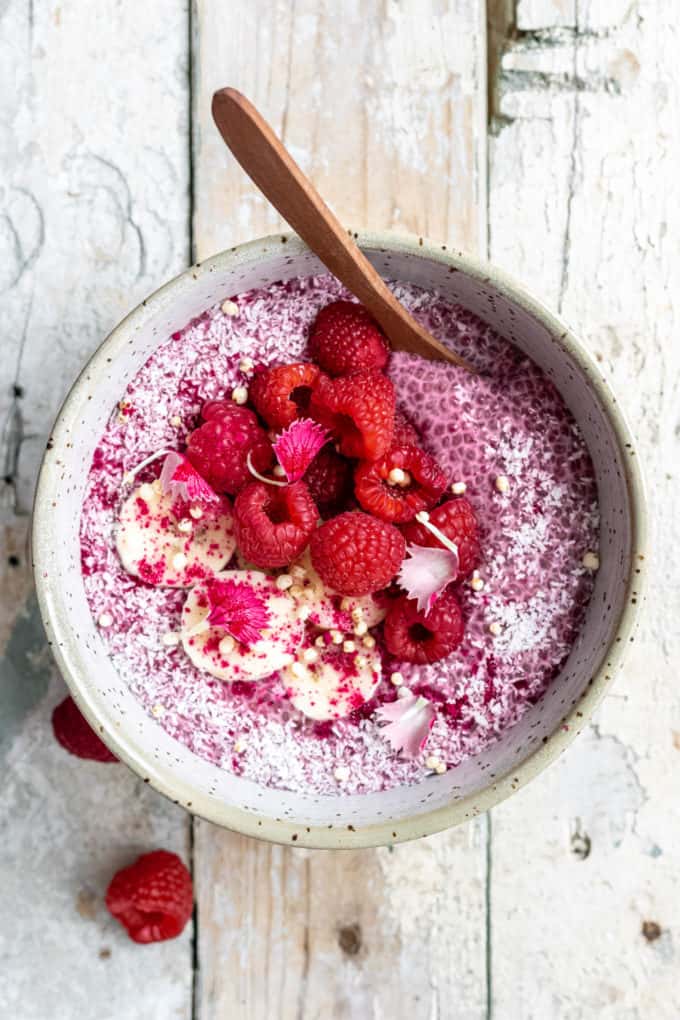 raspberry chia pudding in a white speckled bowl with a spoon in it