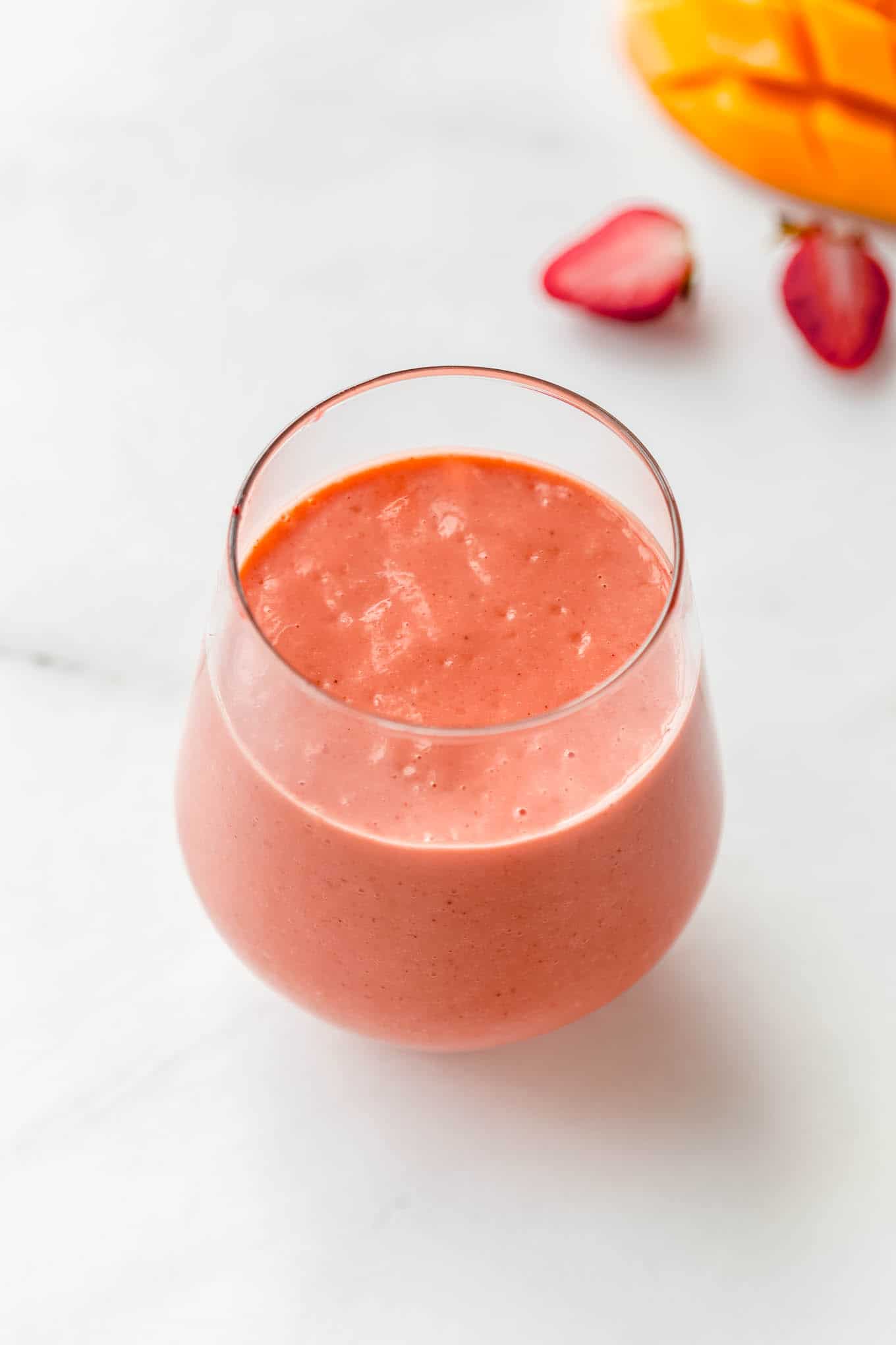 a glass of strawberry mango smoothie on a marble counter