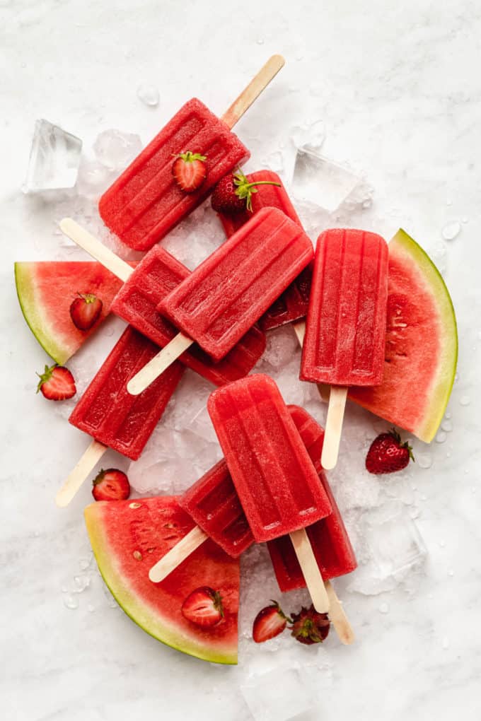 Strawberry watermelon popsicles on a marble board with slices of watermelon