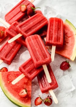 Strawberry watermelon popsicles on ice with strawberries and watermelon around them