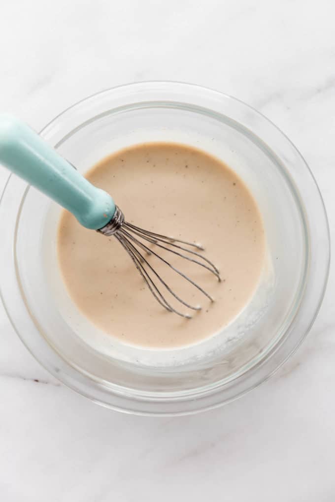 a mixing bowl with lemon tahini dressing and a whisk in it
