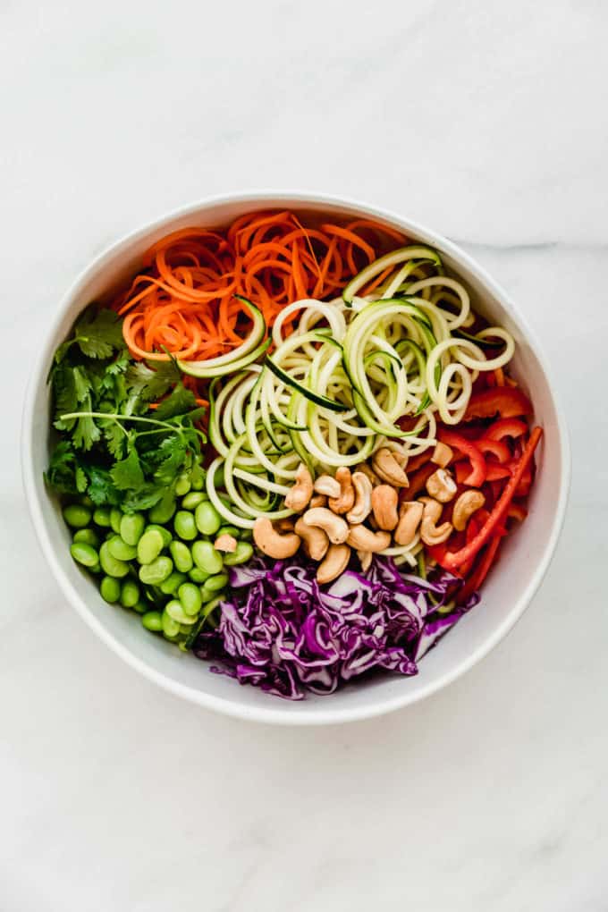 Spiralized zucchini, carrots, peppers, purple cabbage, edamame and cilantro in a bowl
