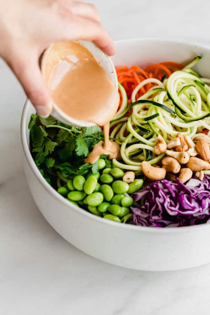 A hand pouring peanut sauce into a bowl on vegeteables