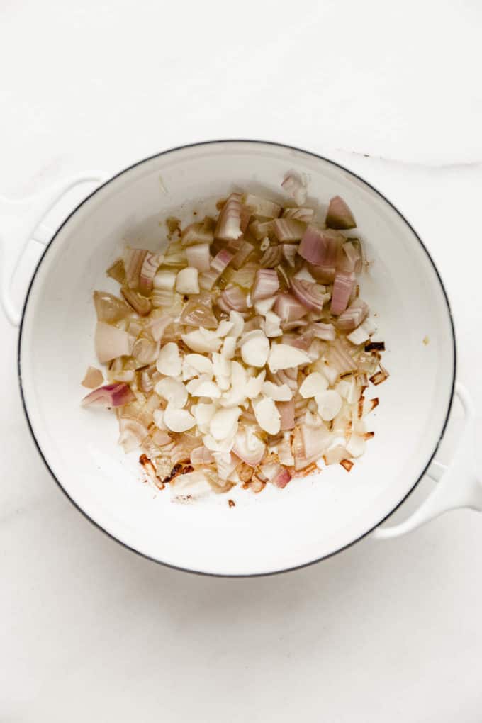 A white pot with shallots and garlic in it