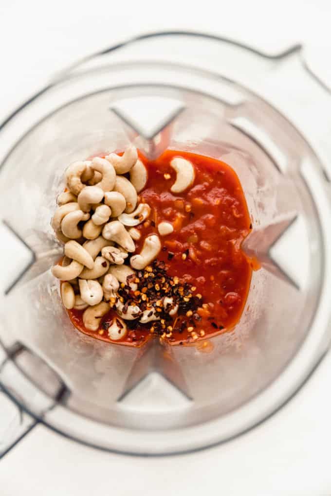 A blender with tomato sauce, chili flakes and cashews in it