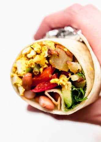 A hand holding a half of a vegan breakfast burrito