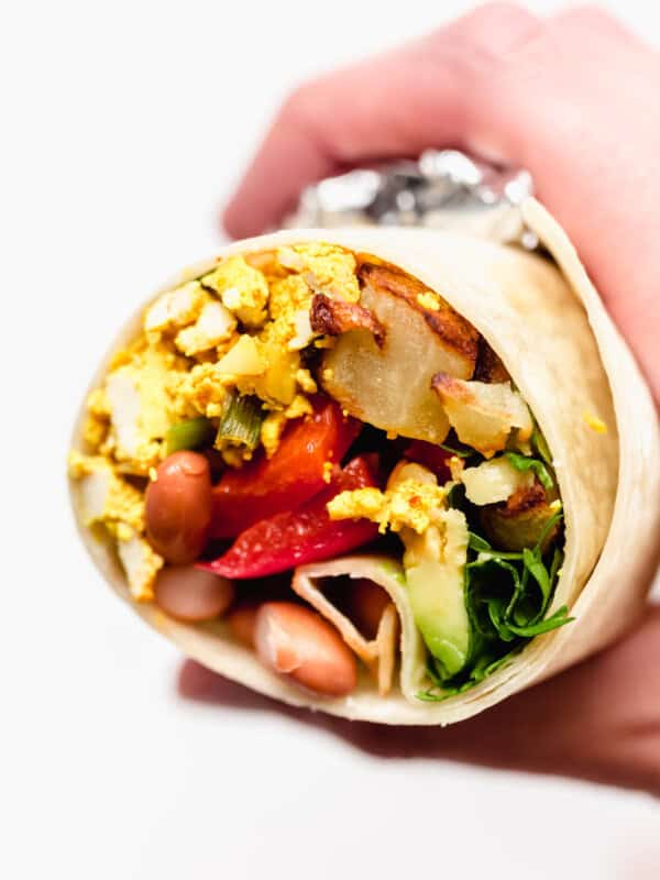 A hand holding a half of a vegan breakfast burrito