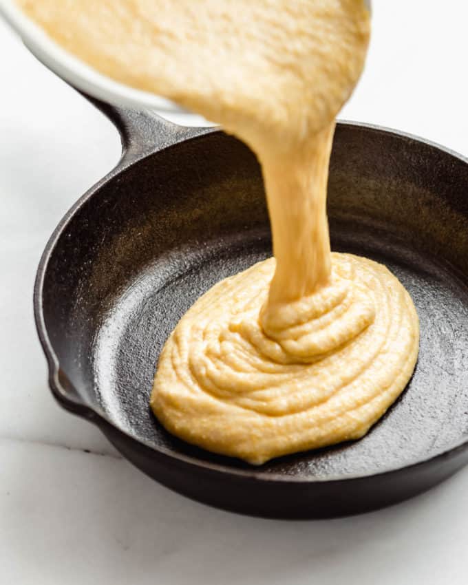 Cornbread batter being poured into a cast iron skillet