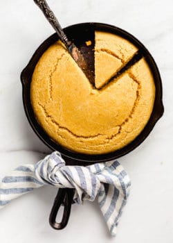 Cornbread in a cast iron skillet with a blue striped napkin tied around the handle