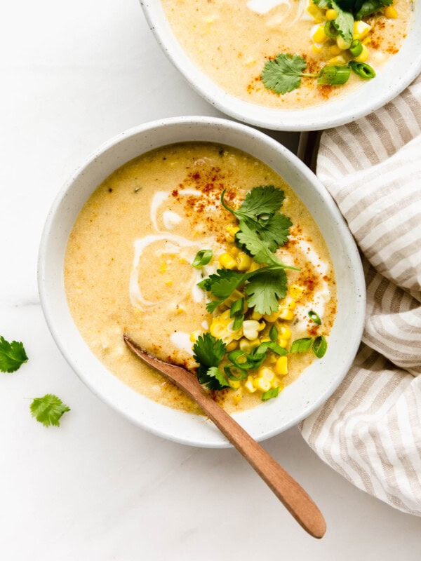A bowl of vegan corn chowder with a wood spoon in it