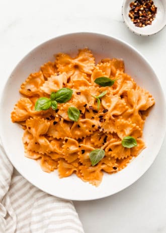 A bowl of vegan vodka pasta with a side of chili flakes and a napkin