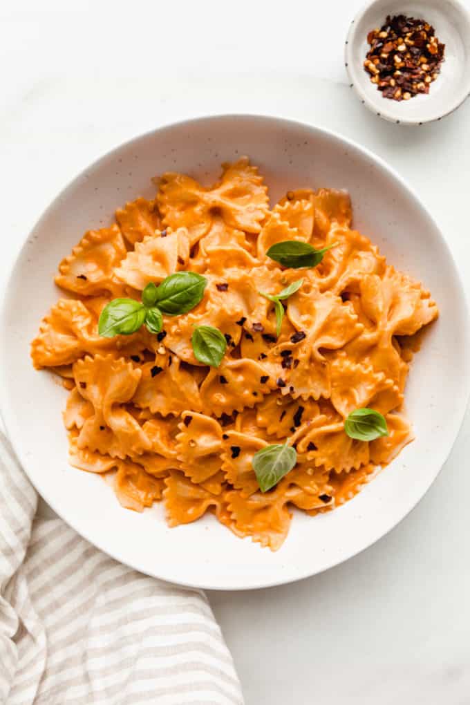 A bowl of vegan vodka pasta with a side of chili flakes and a napkin