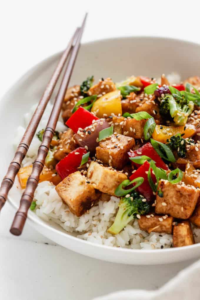 Tofu stir fry in a white bowl with wood chopsticks