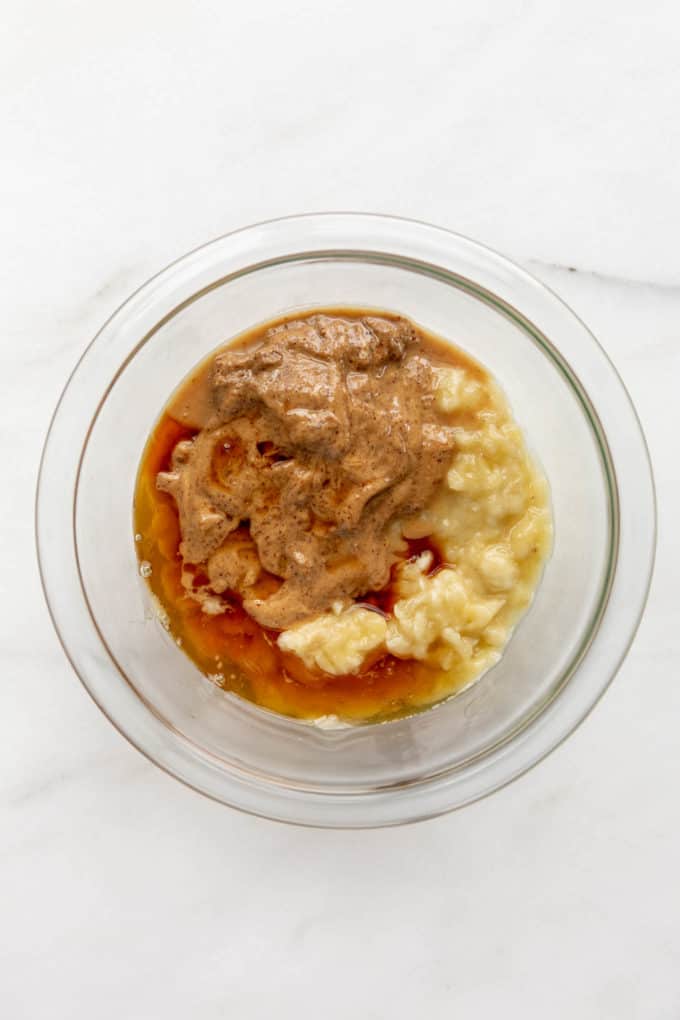 A mixing bowl with mashed banana, almond butter and maple syrup in it