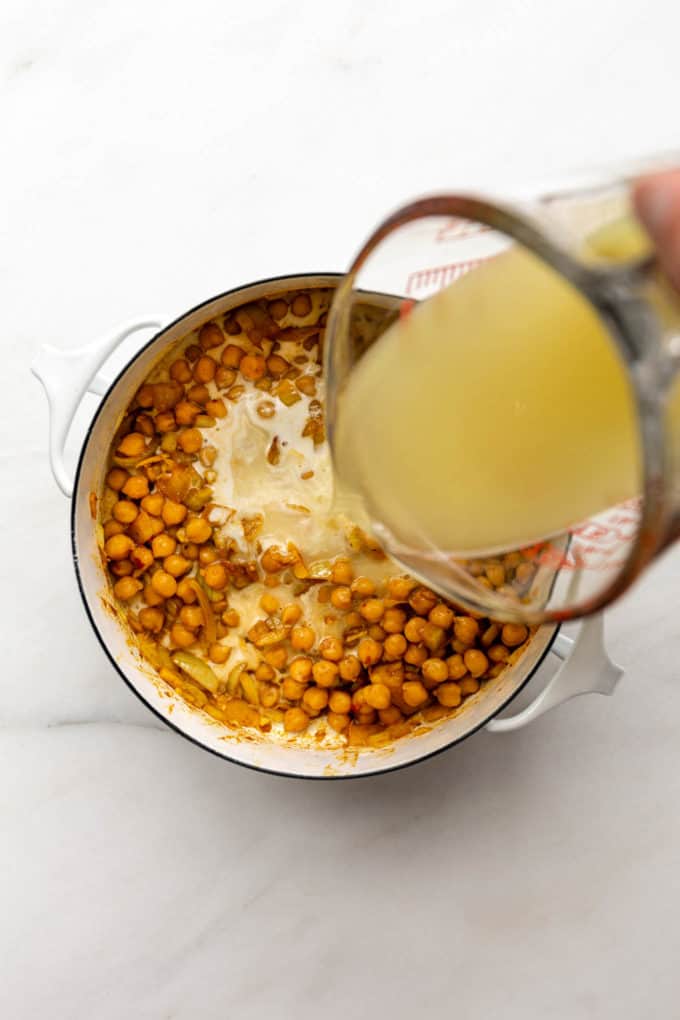 vegetable broth being poured into a pot of chickpeas