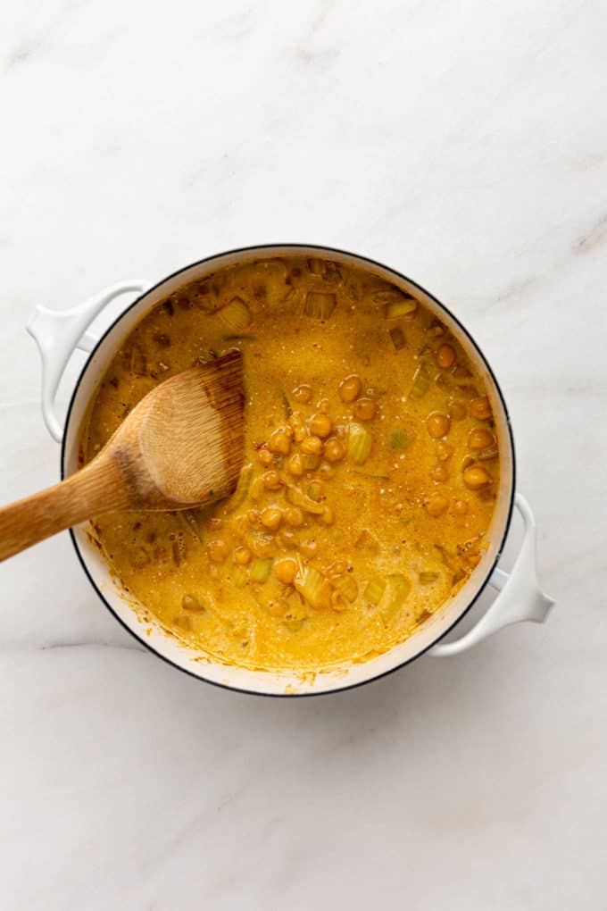 Coconut curry chickpeas being mixed in a pot with a wooden spoon
