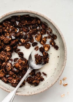 A spoon scooping up chocolate granola and almond milk in a bowl