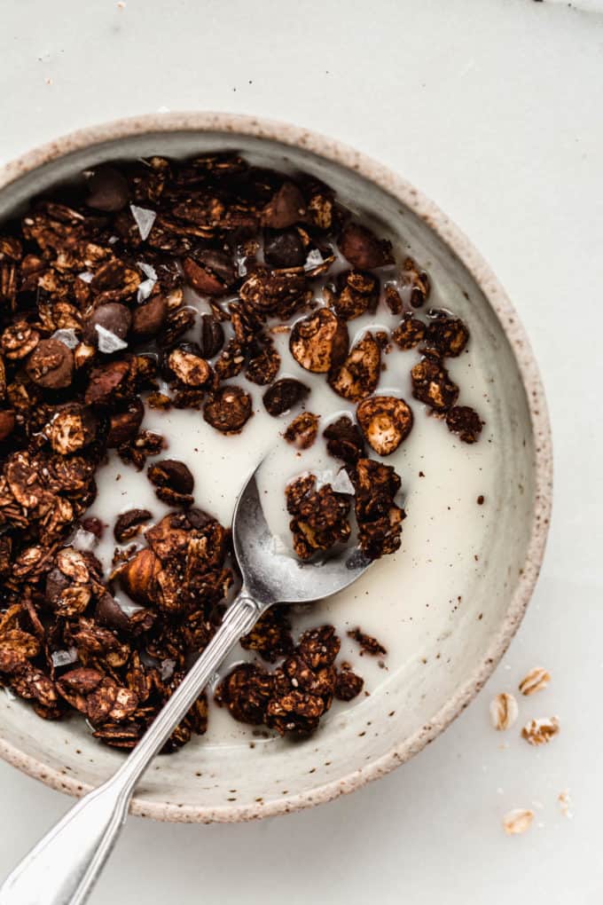 A spoon scooping up chocolate granola and almond milk in a bowl