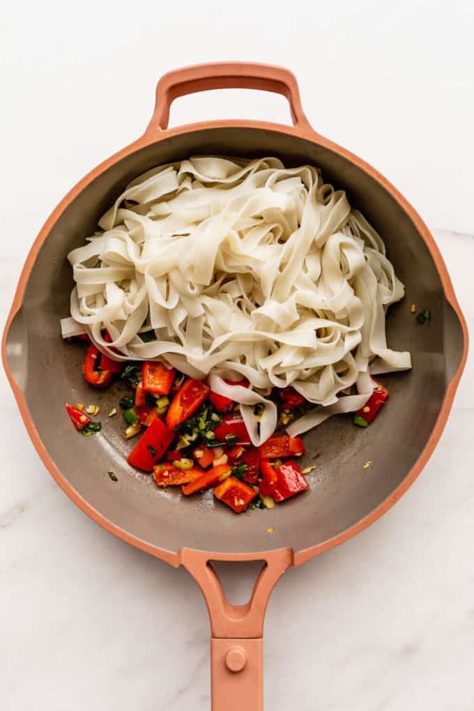 a pan with rice noodles and red peppers in it