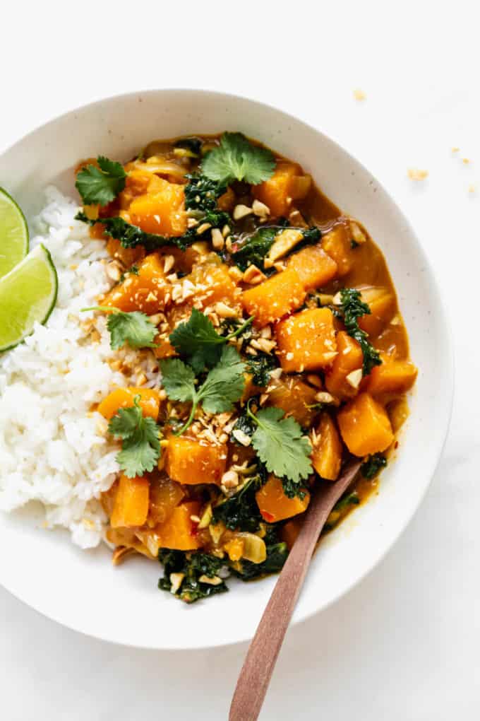 Butternut squash curry in a white bowl with a wood spoon