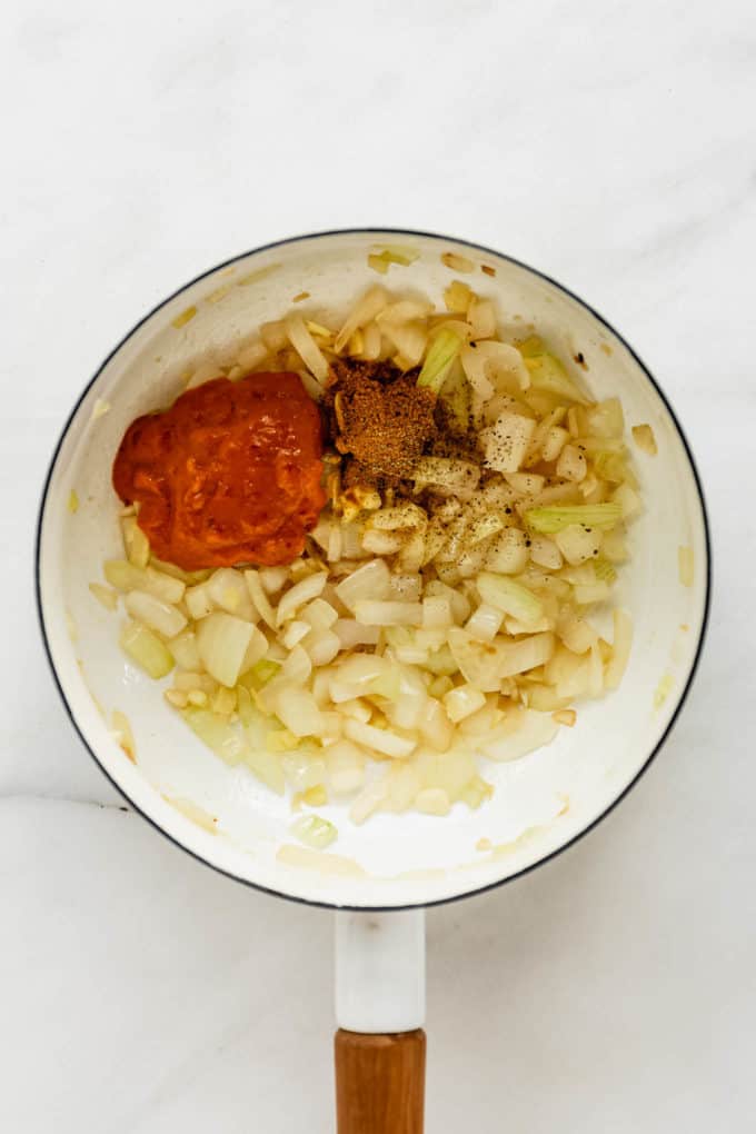 A white pot with onions, garlic and curry paste in it