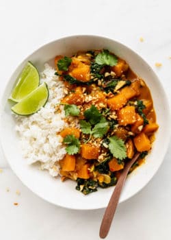 A bowl of butternut squash curry topped with cilantro and a lime wedge