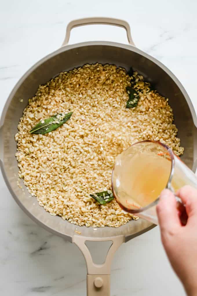 a hand pouring broth into a pan of rice