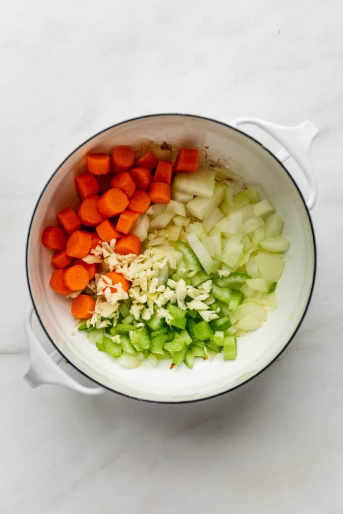 A white pot with carrots, celery, onions and garlic in it