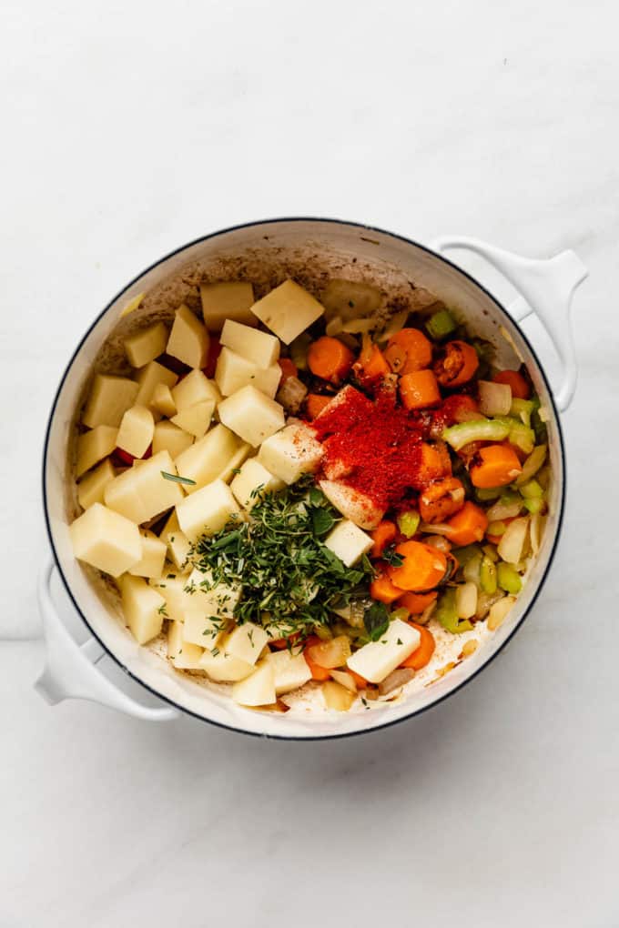 A white pot with potatoes, vegetables and herbs in it