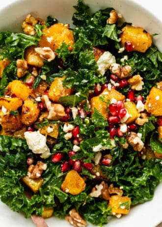 A close up of a kale and pumpkin salad topped with walnuts and pomegranate