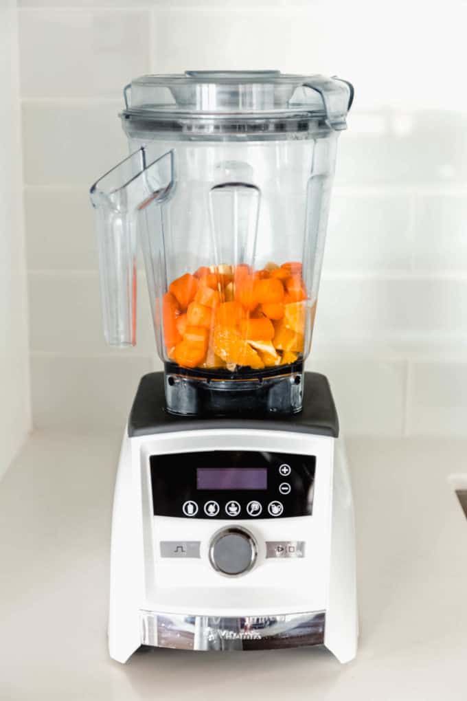 A blender with cut up oranges, carrots and ginger in it