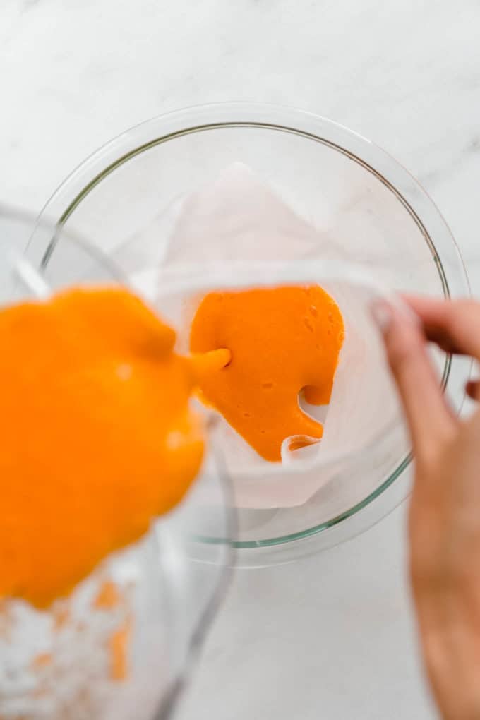 A blender pouring orange, carrot and ginger juice into a mesh straining bag