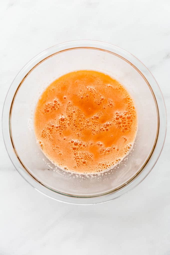 A clear mixing bowl with orange, carrot and ginger juice in it