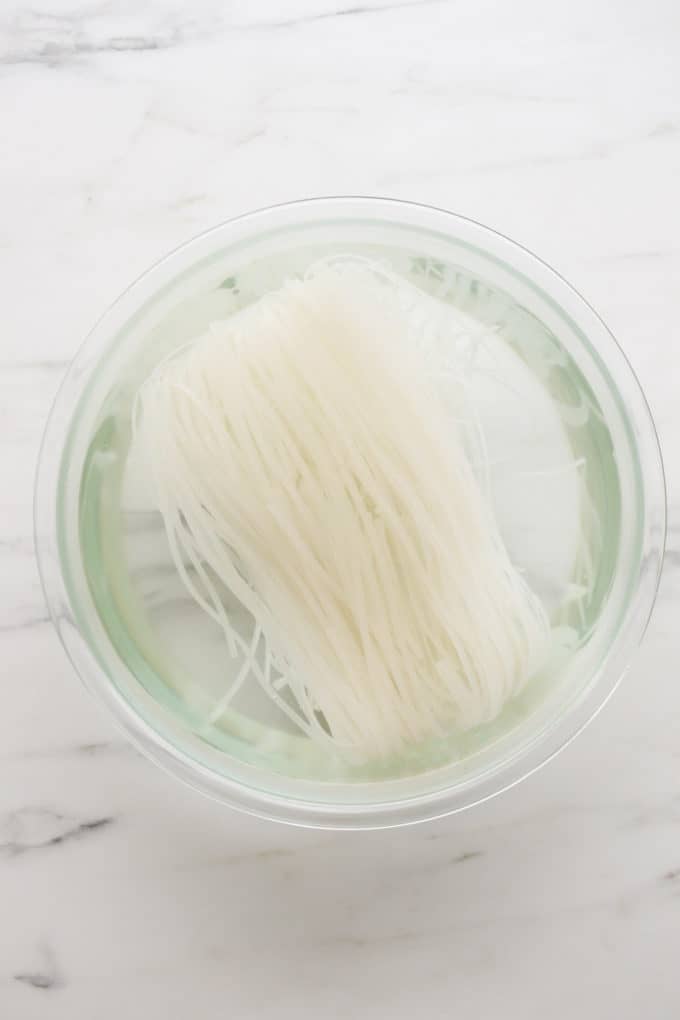 Rice noodles soaking in water in a clear bowl